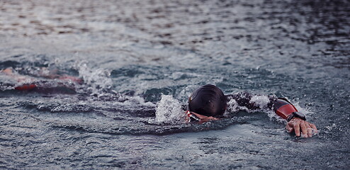 Image showing triathlon athlete swimming on lake in sunrise wearing wetsuit