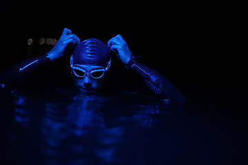 Image showing authentic triathlete swimmer having a break during hard training on night neon gel light