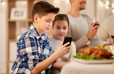 Image showing boy with sister using smartphone at family dinner