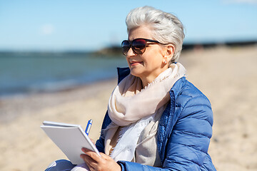 Image showing senior woman writing to notebook on summer beach