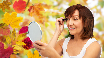 Image showing smiling senior woman with mirror applying mascara