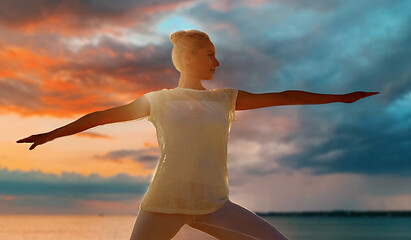 Image showing woman making warrior pose over sea sunset