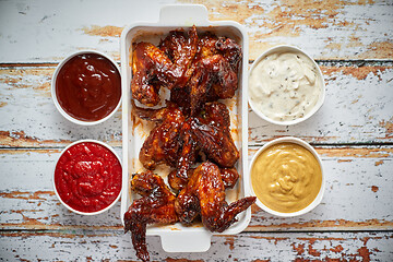 Image showing Chicken wings in thick barbecue sauce with various side dips. Served on white cast iron dish