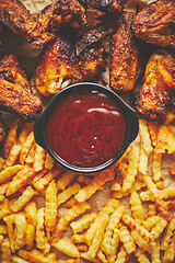 Image showing Appetizing roasted chicken wings and french fries with barbecue dip, served on baking paper