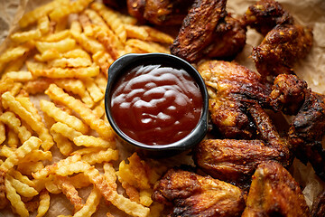 Image showing Appetizing roasted chicken wings and french fries with barbecue dip, served on baking paper