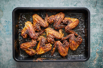 Image showing Grilled chicken wings in spices in black metal baking tray on stone table. Top view