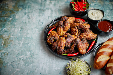 Image showing Grilled chicken wings with chilli pepper on a rustic plate served with various dips and bread