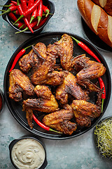 Image showing Grilled chicken wings with chilli pepper on a rustic plate served with various dips and bread