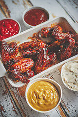 Image showing Chicken wings in thick barbecue sauce with various side dips. Served on white cast iron dish