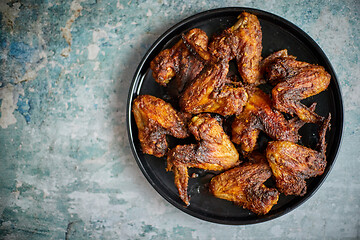 Image showing Grilled chicken wings on a black ceramic plate. Placed on a stone