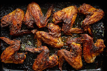 Image showing Grilled chicken wings in spices in black metal baking tray on stone table. Top view