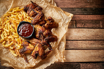 Image showing Appetizing roasted chicken wings and french fries with barbecue dip, served on baking paper