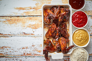 Image showing Chicken wings in thick barbecue sauce with various side dips. Served on white cast iron dish