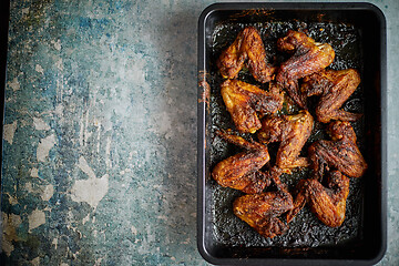 Image showing Grilled chicken wings in spices in black metal baking tray on stone table. Top view