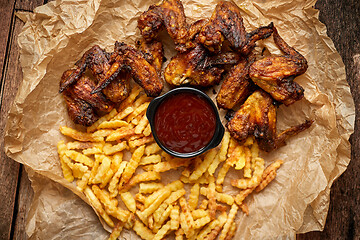 Image showing Appetizing roasted chicken wings and french fries with barbecue dip, served on baking paper