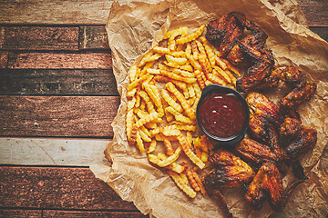 Image showing Appetizing roasted chicken wings and french fries with barbecue dip, served on baking paper