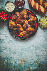 Image showing Grilled chicken wings with chilli pepper on a rustic plate served with various dips and bread