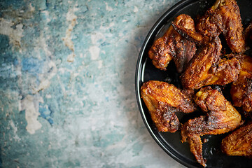 Image showing Grilled chicken wings on a black ceramic plate. Placed on a stone