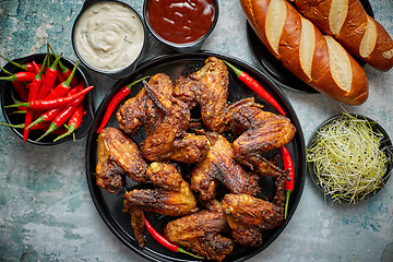 Image showing Grilled chicken wings with chilli pepper on a rustic plate served with various dips and bread