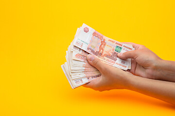 Image showing In hands lies a bundle of five thousandth bills on a yellow background