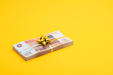 Image showing On a yellow background lies a bundle of notes with a yellow ribbon and a bow