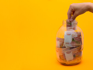 Image showing Hand stuffs a five thousandth bill into a glass jar