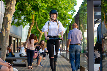 Image showing Trendy fashinable teenager, beautiful blonde girl riding public rental electric scooter in urban city environment. Eco-friendly modern public city transport