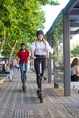 Image showing Trendy fashinable teenager girls riding public rental electric scooters in urban city environment. Eco-friendly modern public city transport