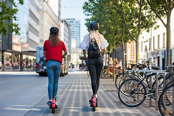 Image showing Rear view of trendy fashinable teenager girls riding public rental electric scooters in urban city environment. New eco-friendly modern public city transport in Ljubljana, Slovenia