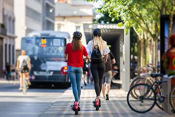 Image showing Rear view of trendy fashinable teenager girls riding public rental electric scooters in urban city environment. New eco-friendly modern public city transport in Ljubljana, Slovenia