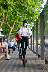 Image showing Trendy fashinable teenager girls riding public rental electric scooters in urban city environment. New eco-friendly modern public city transport in Ljubljana, Slovenia