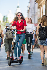 Image showing Trendy fashinable teenager girls riding public rental electric scooters in urban city environment. New eco-friendly modern public city transport in Ljubljana, Slovenia