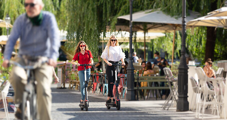 Image showing Trendy fashinable teenager girls riding public rental electric scooters in urban city environment. New eco-friendly modern public city transport in Ljubljana, Slovenia