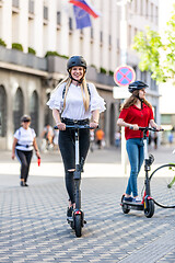 Image showing Trendy fashinable teenager girls riding public rental electric scooters in urban city environment. New eco-friendly modern public city transport in Ljubljana, Slovenia