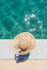 Image showing Woman wearing big summer sun hat relaxing on pier by clear turquoise sea.