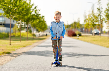 Image showing happy little boy riding scooter in city