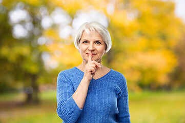 Image showing senior woman making shush gesture in autumn park