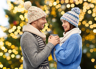 Image showing happy couple holding one cup over christmas lights