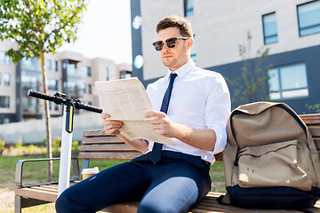 Image showing businessman with scooter reading newspaper in city