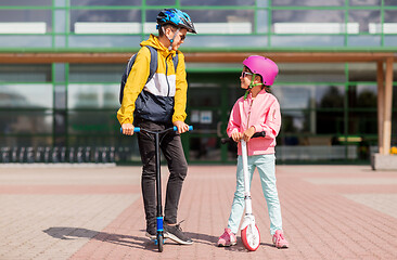 Image showing happy school children in helmets riding scooters