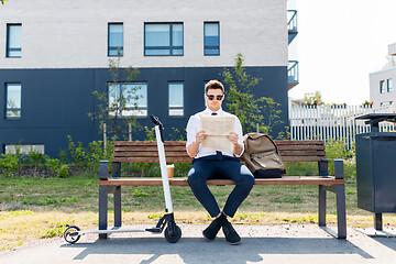 Image showing businessman with scooter reading newspaper in city