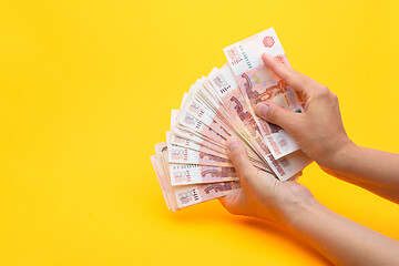 Image showing Hands count money in a bundle of notes, yellow background