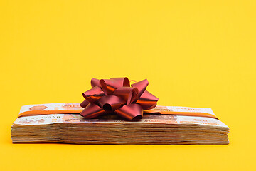 Image showing A bundle of money tied with ribbons and bow on a yellow background