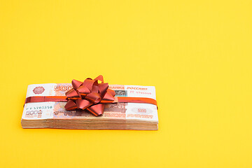 Image showing Gift pack tied with a red bow of five thousandth Russian bills on a yellow background