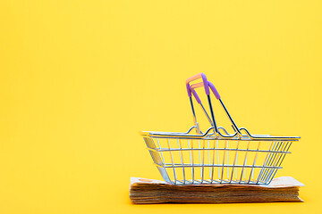 Image showing On a bundle of notes lies an empty grocery basket with raised handles