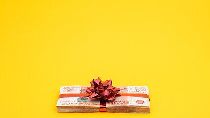 Image showing A pack of five thousandth bills with red ribbons and a bow on a yellow background