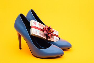 Image showing on a yellow background are women\'s shoes on which five-thousandth bills lie