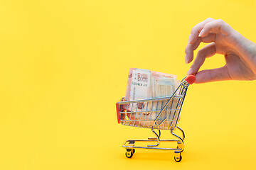 Image showing Hand holds the handle of a grocery cart with a pack of five thousandth Russian rubles, yellow background