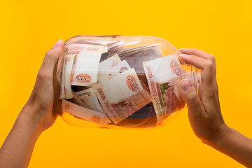 Image showing Hands holding a three-liter jar in which lie five thousandth bills, yellow background