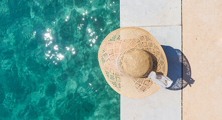 Image showing Woman wearing big summer sun hat relaxing on pier by clear turquoise sea.